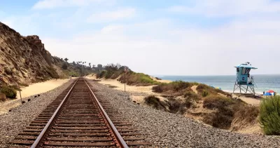 View looking down train tracks at San Clemente, California with grassy beach dunes and blue lifeguard tower on right side.