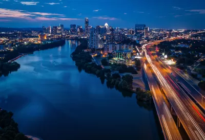 Aerial view of Interstate 35 with blurred traffic and Austin, Texas skyline in background with river in foreground at nighttime.
