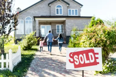 'For sale' sign with 'Sold' update in front of large single-family home with family of three walking toward house.
