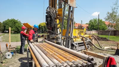 Workers next to excavator digging a geothermal well.