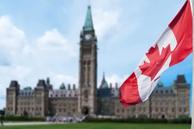 Canadian flag in foreground with blurred Canadian Parliament building in background in Ottawa, Ontario, Canada.