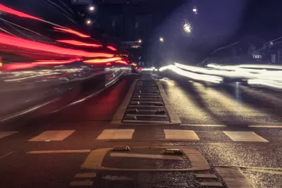 Low view of empty crosswalk at night from middle of street with blurred cars speeding by on both sides.
