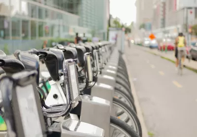 Close-up of silver Bixi bike share bikes parked at a station in Montreal, Quebec, Canada with blurred person on bike riding away in background.