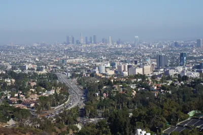 Downtown Los Angeles skyline viewed from a distance with freeway and trees in foreground.
