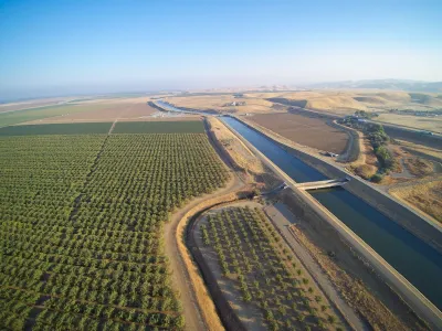 Aerial view of Claifornia aqueduct with green orchard on one side.
