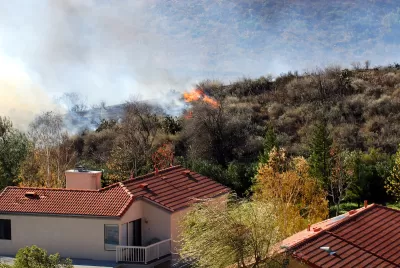 Wildfire approaching stucco house with red tile roof.