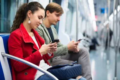 Young woman and man seated on subway car looking at phones.