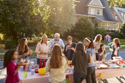 Group of people standing around a table with food in front of homes during a block party.
