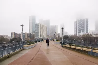 One cyclist rides on pedestrian bridge with foggy Austin, Texas skyline in background.