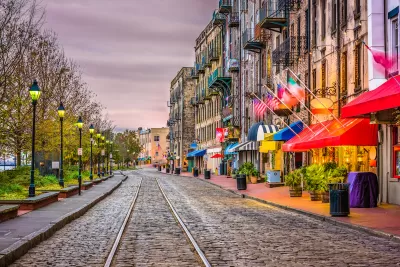 Cobblestone street with streetcar line, row of vintage streetlights on left, and colorful restaurant and shop awnings on right on River Street in Savannah, Georgia.