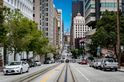 View from middle of street with streetcar rails and high-rise buildings on either side in San Francisco, Bay Bridge visible in background
