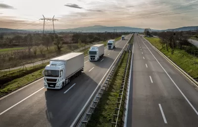 Aerial view of a line of freight trucks driving on a country highway.