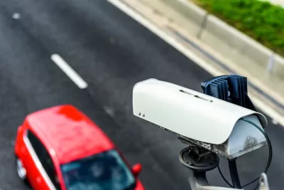 Close-up of speed camera mounted above roadway with red car passing by underneath