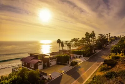 View of oceanfront homes in Malibu, California against golden afternoon sky