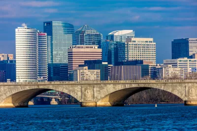 Washington D.C. office buildings with river and stone arched bridge in foreground.