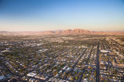 Aerial view of sprawling Las Vegas suburbs at golden hour with desert mountain in background.