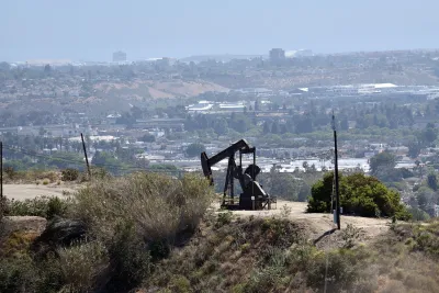 Oil well on hilltop in Los Angeles with city neighborhoods in background.
