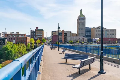 Pedestrian bridge with benches in Rochester, New York with brick buildings in background.