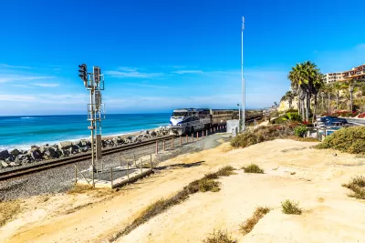 Silver and blue train passing by on track at the edge of Pacific Ocean in San Clemente, California.