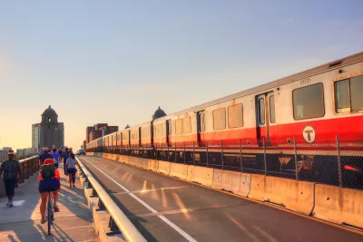 Cyclists and a red T train on the Longfellow Bridge in Boston, MA at sunset.