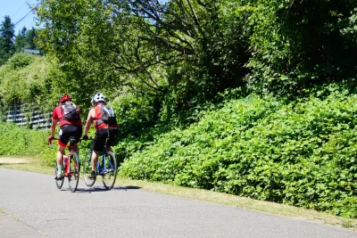 Two people on bikes riding down paved Burke-Gilman bike trail in King County, Washington on a sunny day.