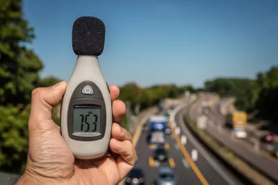 Close-up of hand holding up decibel meter with blurred highway with traffic in background