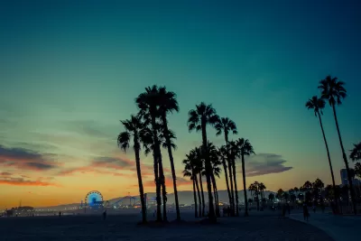Palm trees sillhouetted against dark evening sky at Santa Monica Beach with pier with illuminated Ferris wheel in background.