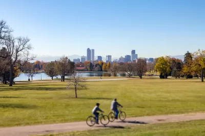 Two people on bikes on trail on green lawn with Denver, Colorado skyline in background.