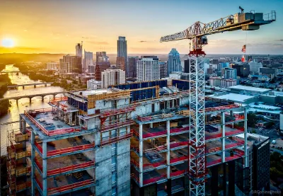 Large tower under construction with crane with American and Texas flags in downtown Austin, Texas against sunset sky.