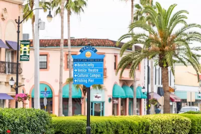 Street sign in Venice, Florida planned community with pink Italianate buildings and palm trees in background.