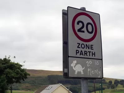 Close-up of white 20 kph speed limit sign in Europe with cartoon turtle and '20 is plenty' sticker underneath.