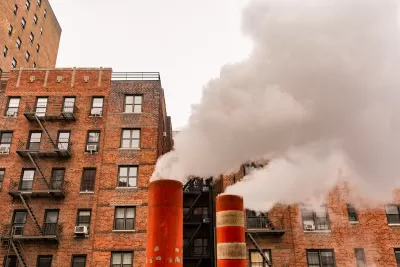 Orange and white steam pipes in New York City releasing white steam against background of red brick buildings.