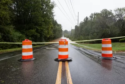 Orange and white barrels with yellow caution tape blocking flooded road.