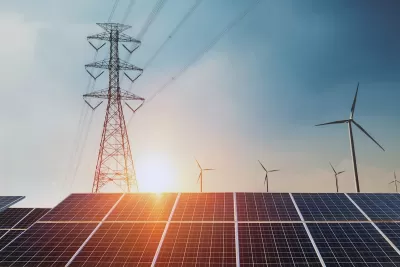 Solar panels, wind turbines, and power line tower against sunset sky.