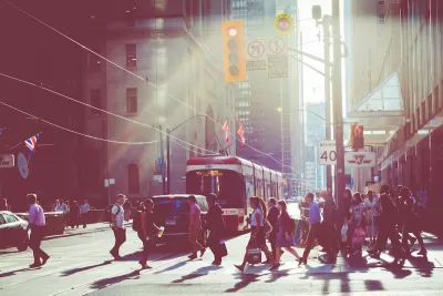 Pedestrians in busy crosswalk with tram in background in downtown Toronto, Canada with sunrise or sunset light in background.