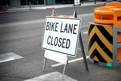 "Bike Lane Closed" A-frame sign on street with yellow and black barricade behind it.