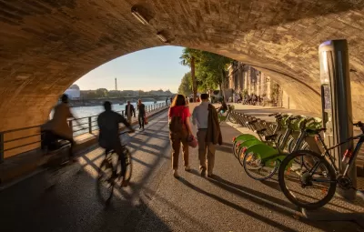 PEople on bikes, pedestrians, and a bike share station under Pont Neuf in Paris, France.