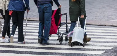 Elderly people wheeling a wheelchair and grocery cart in crosswalk.