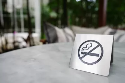 Close-up of silver sign indicating 'no smoking' with cigarette inside circle with line. Sign is sitting on patio table outdoors.