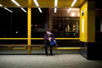 Yellow bus shelter with one young person sitting on bench at night.