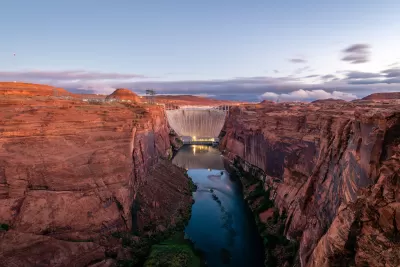 View of Glen Canyon Dam with vertical red stone cliffs on either side, Colorado River at bottom, and dusk sky in background.