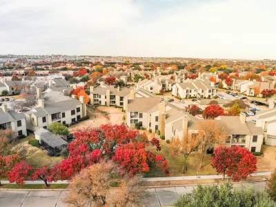 Aerial view of large complex of apartment buildings surrounded by fall foliage trees in suburban Dallas, Texas.
