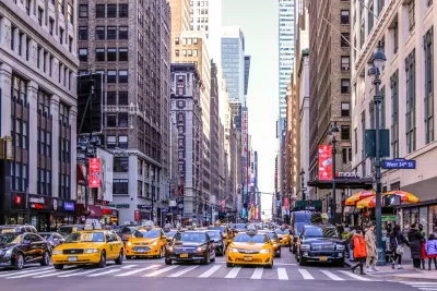Intersection on Manhattan street with yellow cabs and black cars waiting for stoplight.