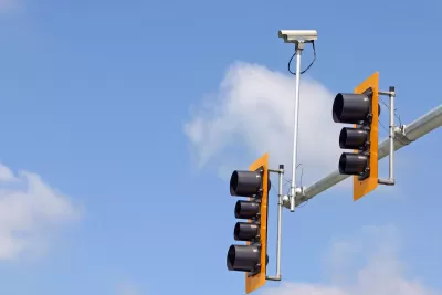 Yellow and black stoplights on horizontal post with small traffic camera.
