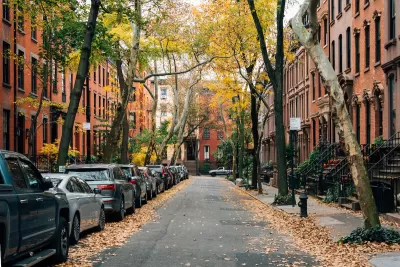 Small New York City street with brownstone homes and cars parked on one side.