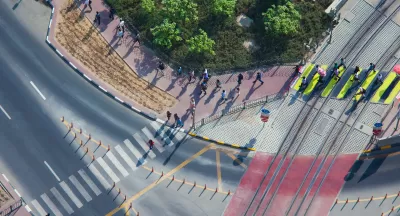 Overhead view of doxens of commuters walking on sidewalk and crossing street in full sun.