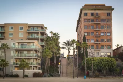 Vintage multi-story brick apartment building and modern concrete and glass apartment building separated by a steep public stairway in Los Angeles, California.