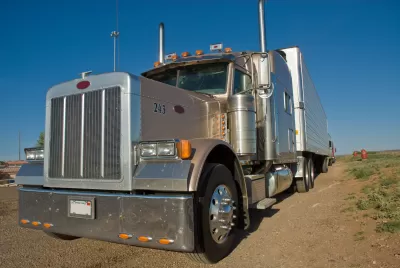 Front view of a tan semi-truck cab parked on a vacant piece of land with a clear blue sky in the background.