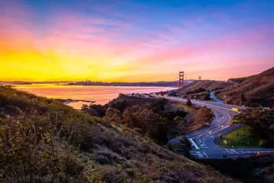 View of windy road in Marin County and Golden Gate Bridge and San Francisco skyline in background at sunrise.
