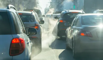 Cars in busy traffic with emissions visible from exhaust pipes.